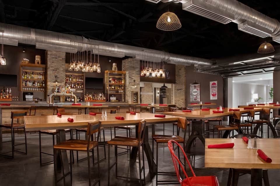 Modern restaurant bar with exposed brick, wooden tables, pendant lighting, and red accents