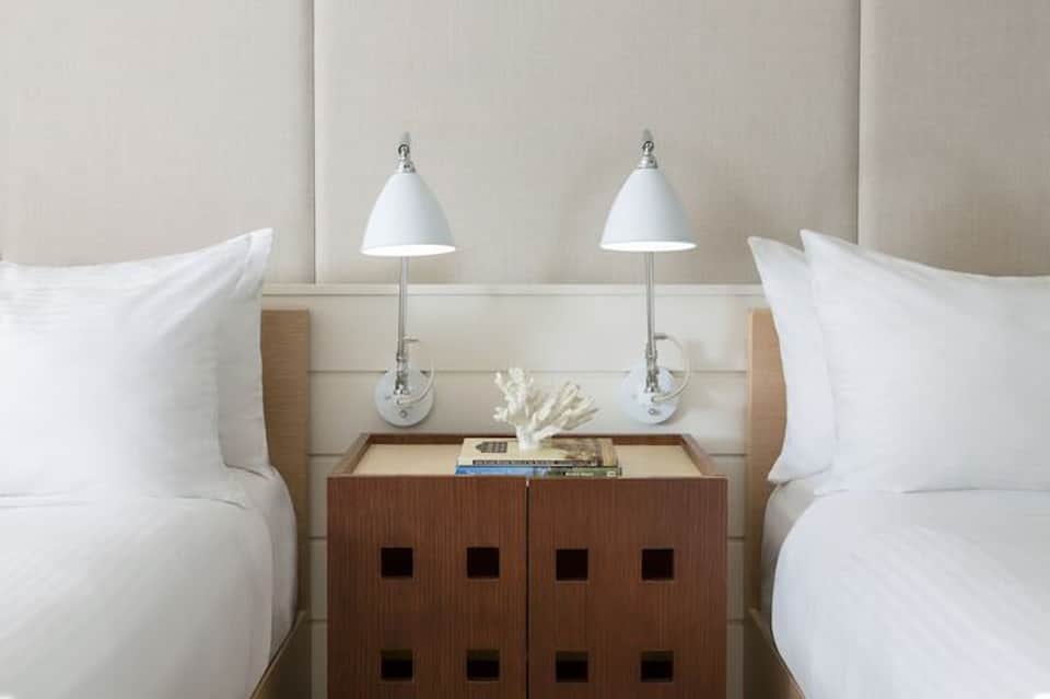 Twin beds with beige headboard, white pillows, and wooden nightstand
