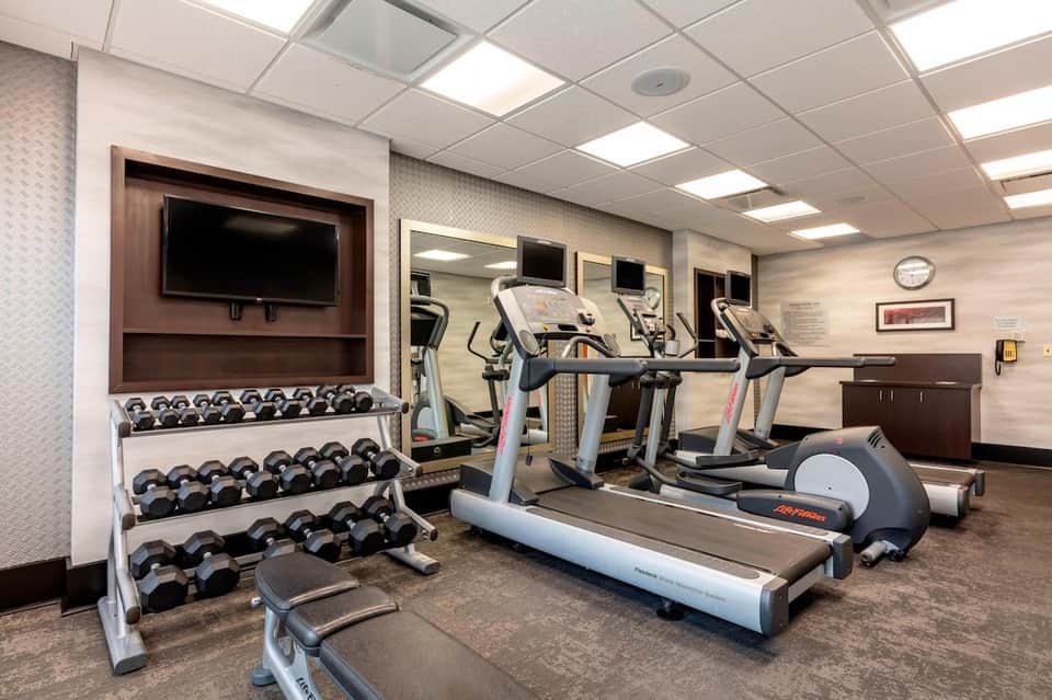 Fitness center with cardio equipment, weights, dumbbells, and TV monitor