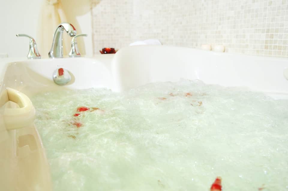 Luxurious bathtub filled with bubbles and rose petals with chrome faucet and tile walls