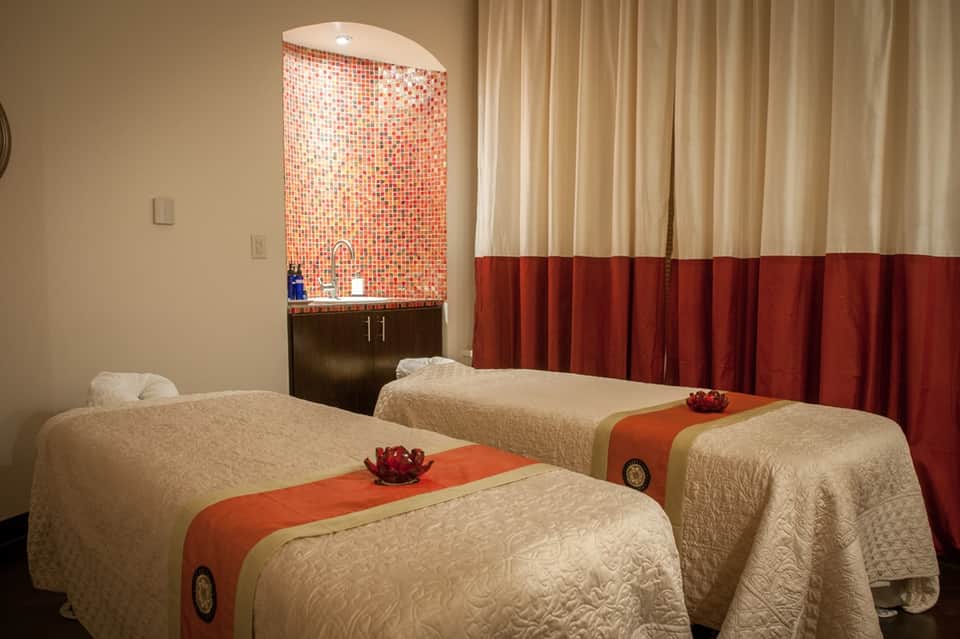 Spa treatment room with two massage beds, mosaic tile feature wall, and elegant curtain partitions