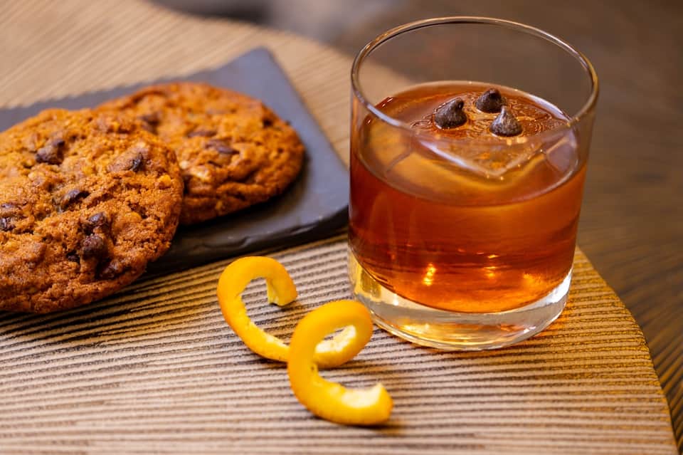 Chocolate chip cookies and amber cocktail with citrus peel on wooden table