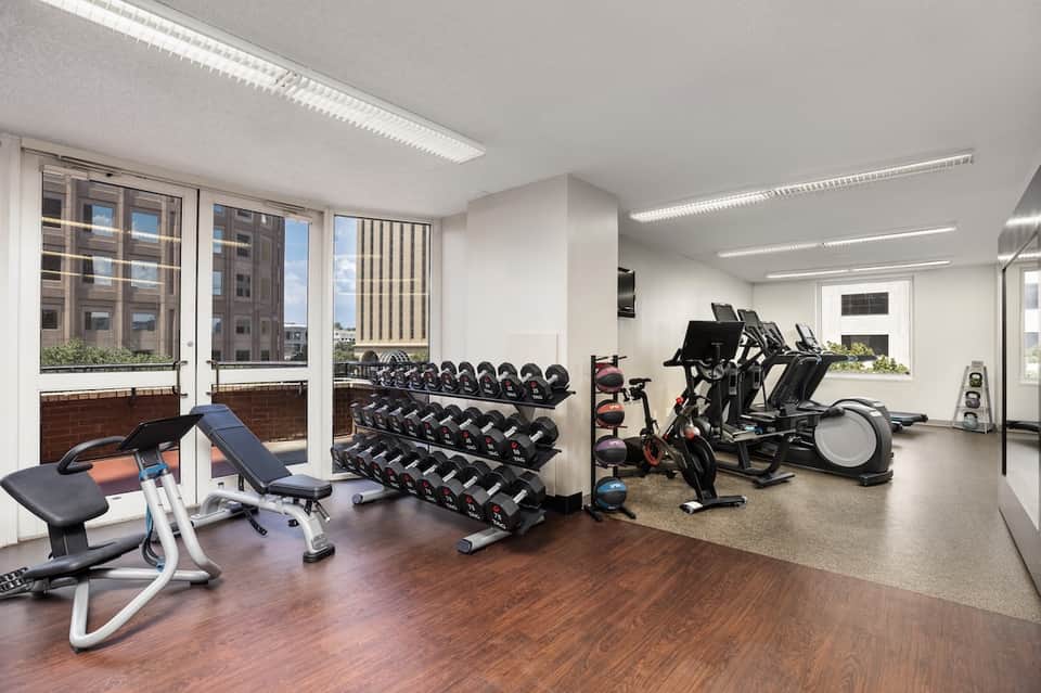 Modern fitness center with dumbbells, stationary bikes, exercise equipment, and city views