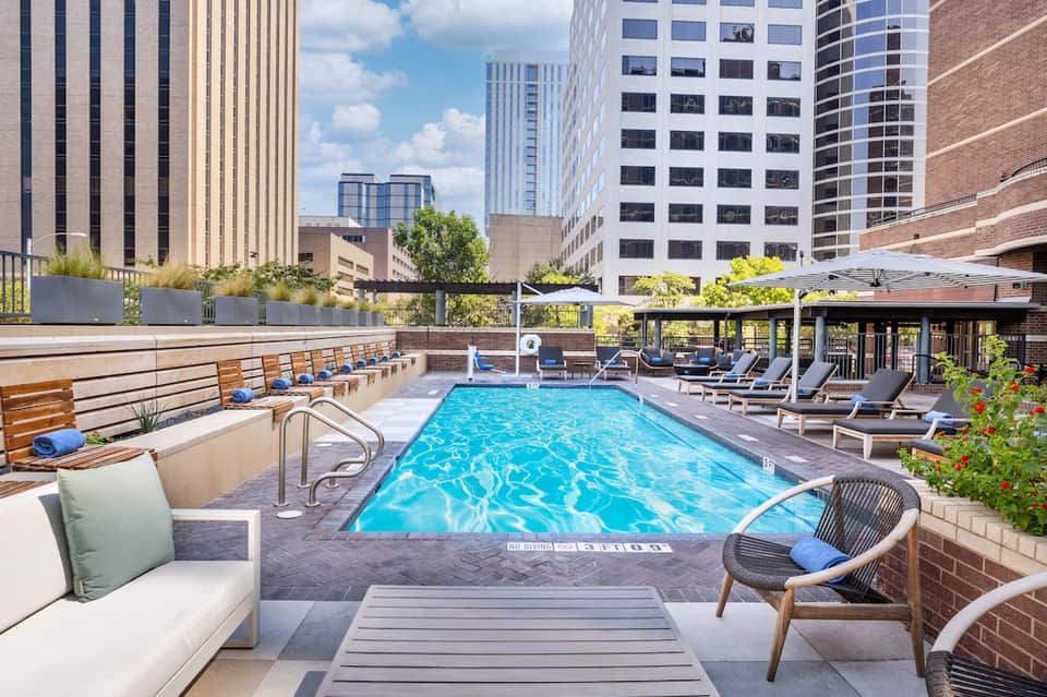 Rooftop pool with turquoise water, city skyline views, loungers, umbrellas, and modern urban setting