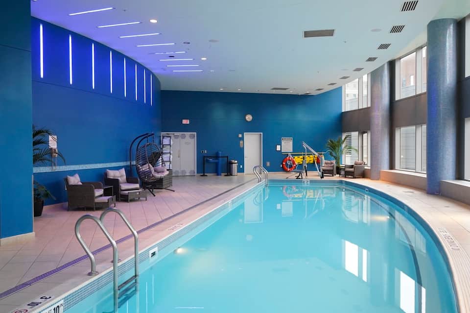 Indoor pool facility with bright blue walls, neon lighting, lounging area, and large windows