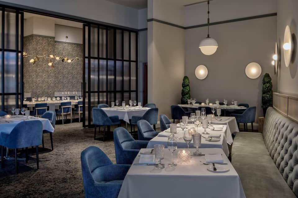 Upscale fine dining restaurant with blue accent chairs, white tablecloths, and elegant pendant lighting