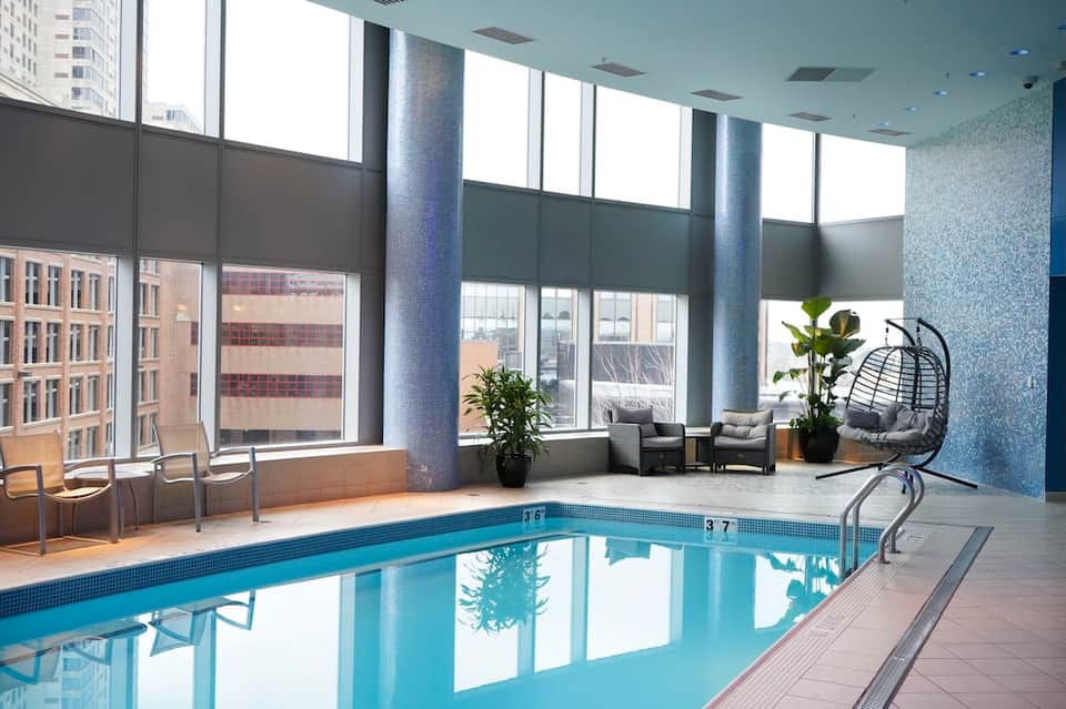 Indoor heated swimming pool with floor-to-ceiling windows and modern lounge seating area