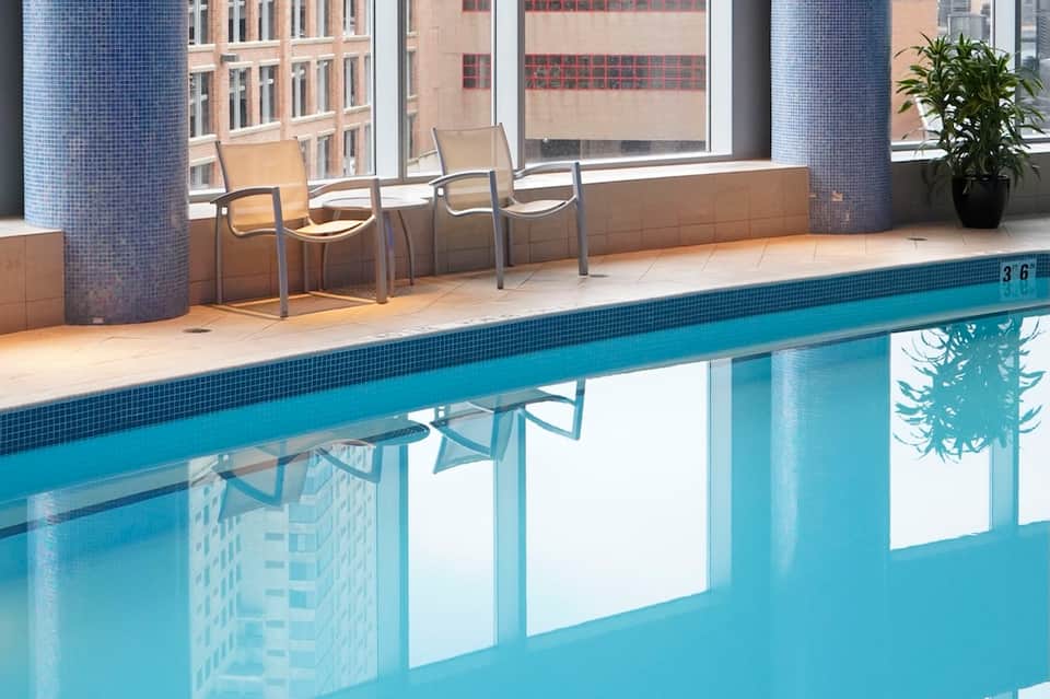 Indoor pool with blue water, large windows overlooking city, modern deck seating area
