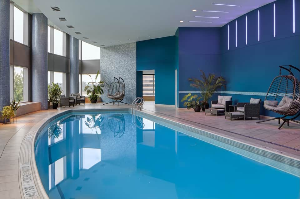 Modern indoor pool facility with blue water, tall windows, and contemporary lounge seating