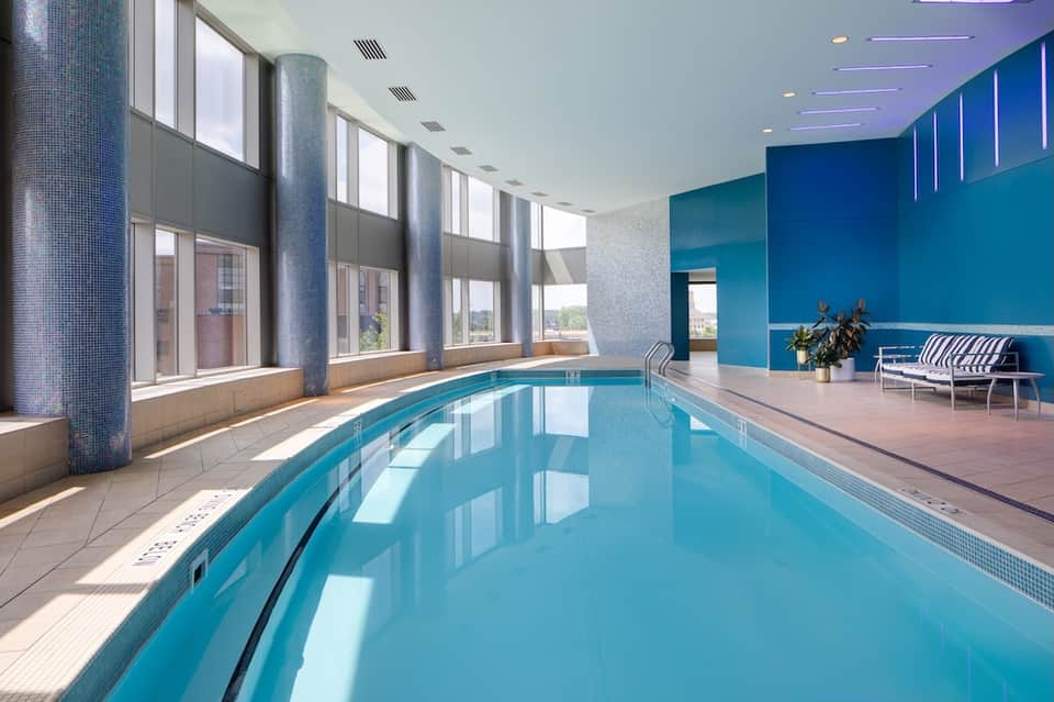 Indoor heated pool with blue water, large windows, blue accent walls, and modern architectural columns
