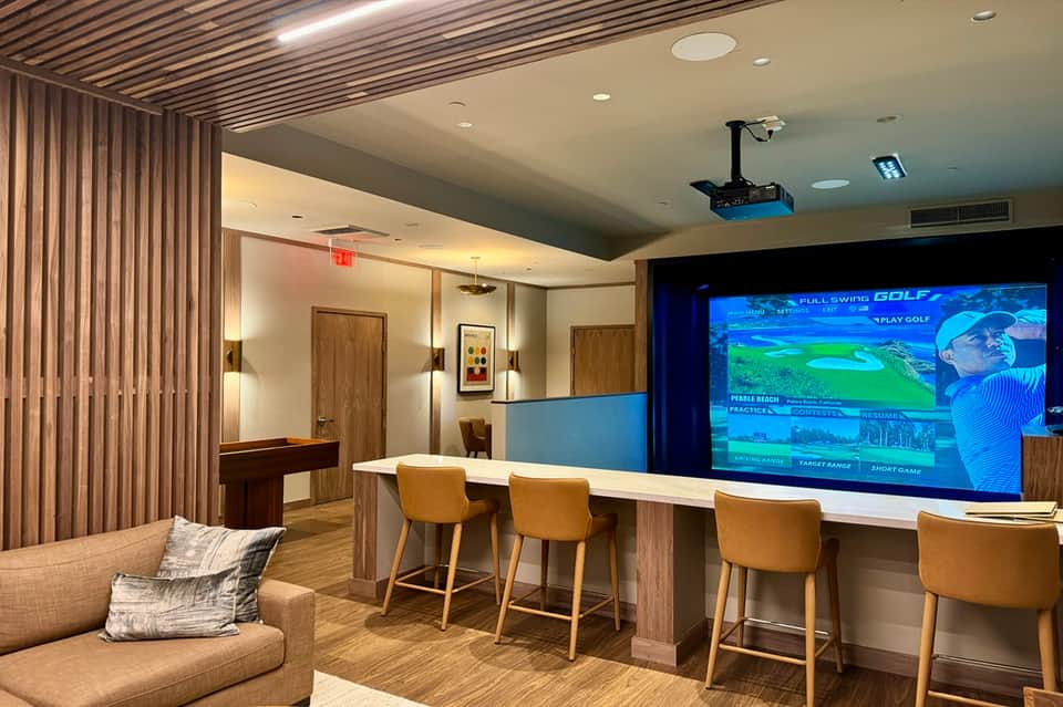 Game room with golf simulator screen, bar seating, and wood paneling
