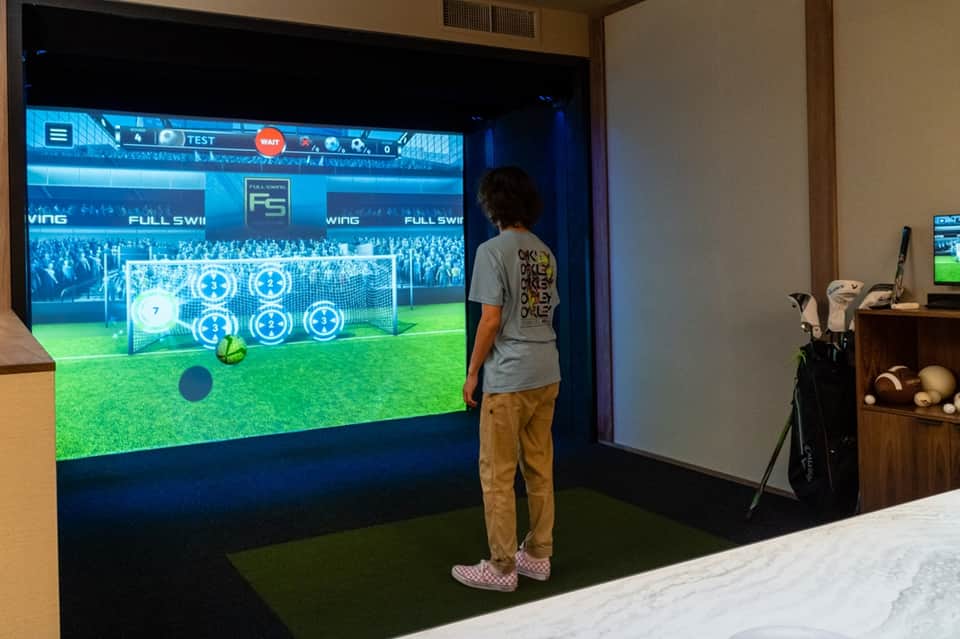 Man using interactive golf simulator screen with virtual course display and golf equipment nearby