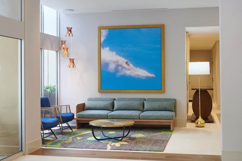 Hotel lobby seating area with gray sofa, blue accent chair, framed artwork, hanging copper pendant lights