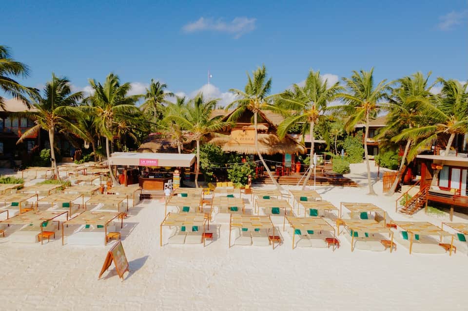 Beachfront resort gathering space with wooden chairs arranged on white sand and palm trees