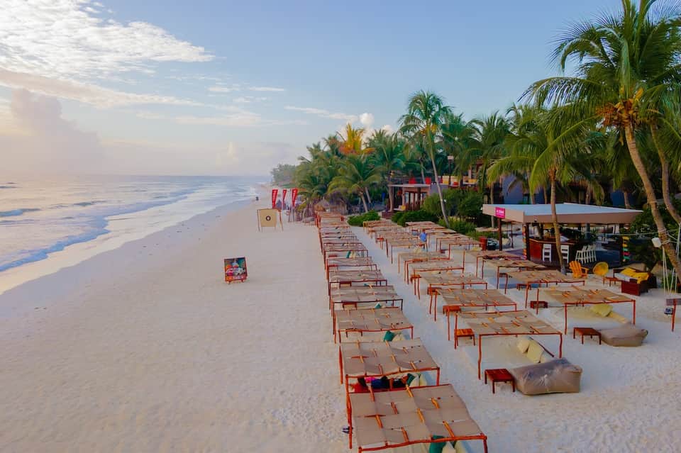 Beach resort with palm trees, colorful structures, and lounge beds on white sand shore