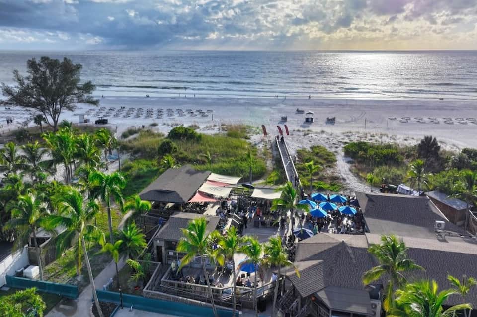 Beachfront resort with umbrellas on sand, palm trees, and ocean boardwalk