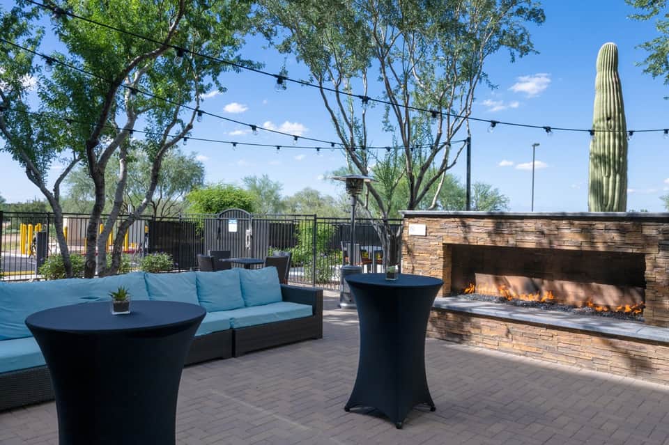 Desert patio with blue lounge seating, fireplace, saguaro cactus, string lights, and mountain views