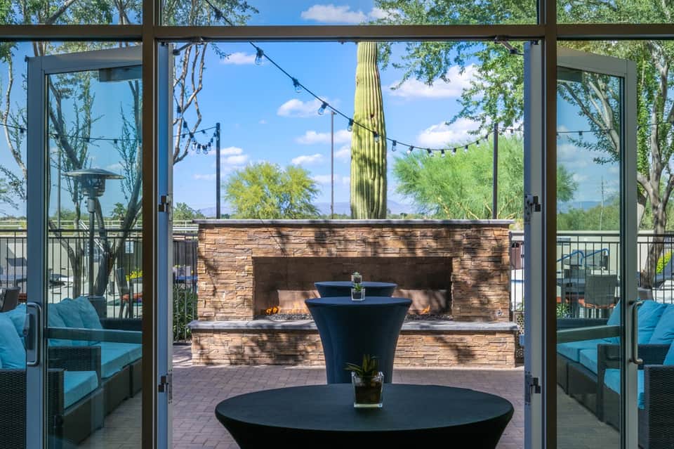 Modern lounge area with large windows overlooking fireplace, patio seating, and desert landscape