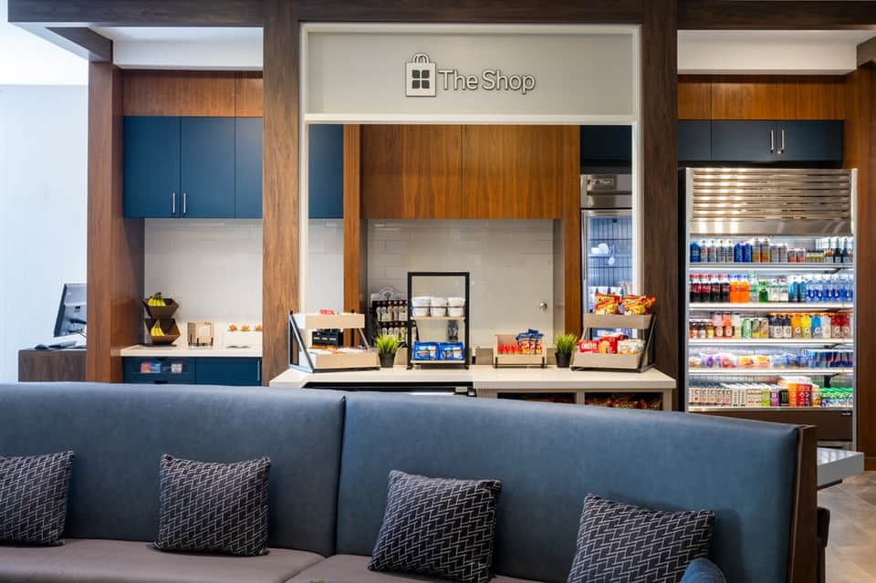 Hotel lobby with The Shop retail area featuring wood cabinetry, blue accents, and beverage refrigerator display
