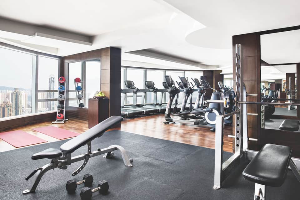 Modern high-rise fitness center with rows of exercise bikes, treadmills, and dumbbells with panoramic city views