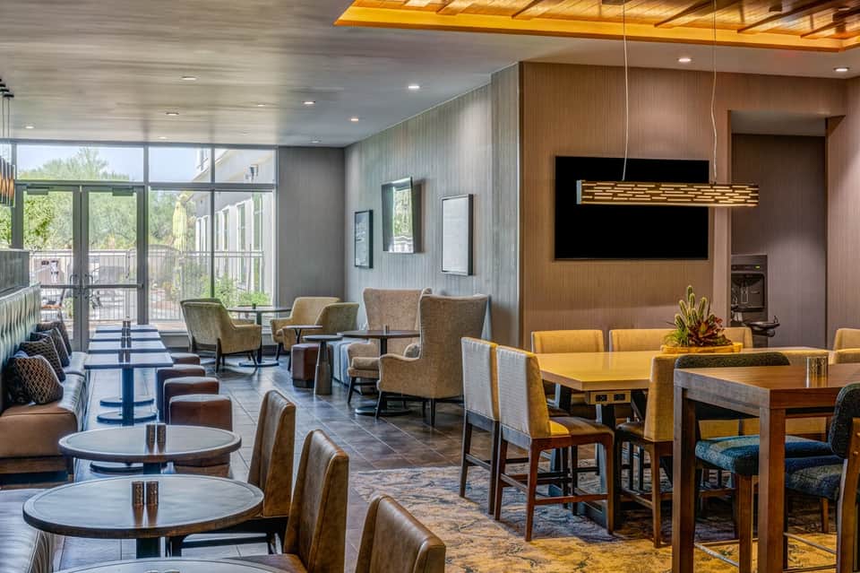 Modern hotel lounge with wooden accents, comfortable seating, dining tables, and floor-to-ceiling windows