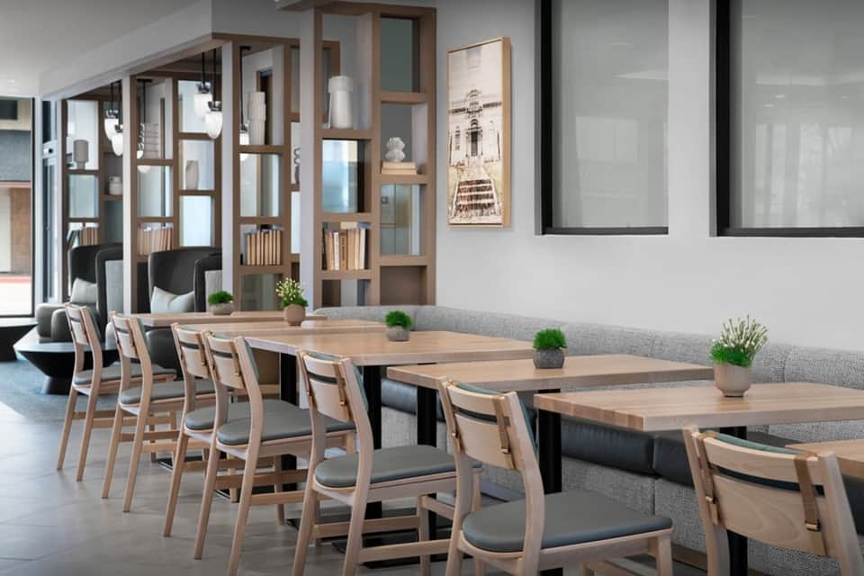 Modern meeting room with long wooden tables, light wood chairs, and glass partitions