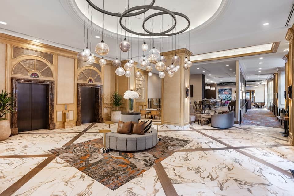 Elegant hotel lobby with marble floors, glass chandelier, dark wood doors, and seating
