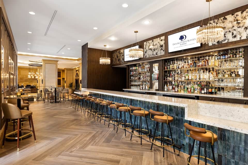 Upscale hotel bar with marble countertop, extensive liquor selection, and elegant chandeliers