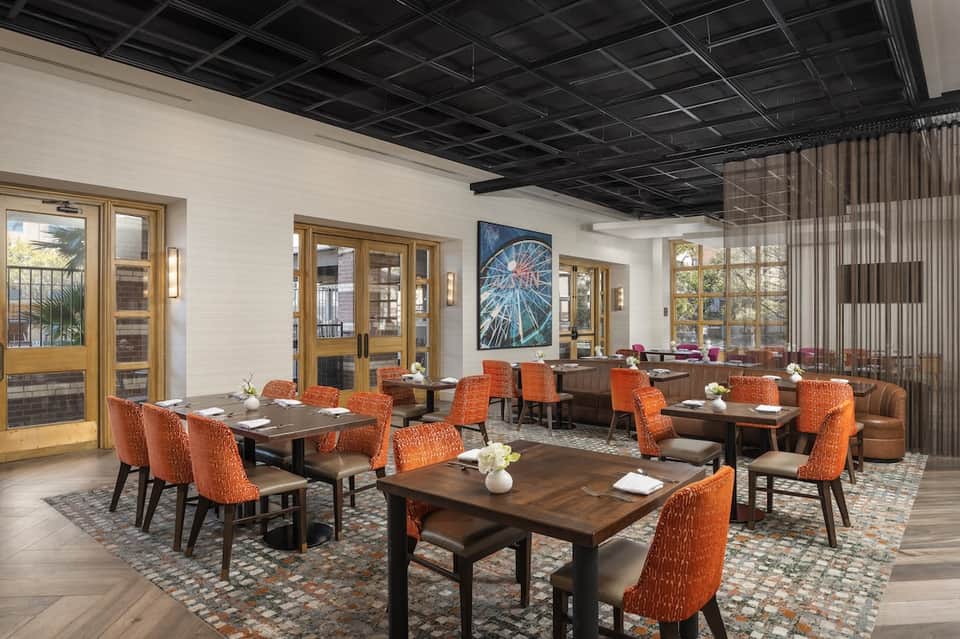 Contemporary hotel restaurant with wood tables, orange chairs, and large windows