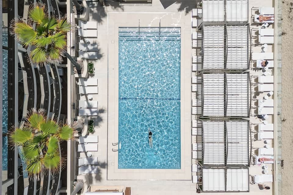 Aerial view of rectangular hotel pool with lounge chairs and palm trees surrounding deck