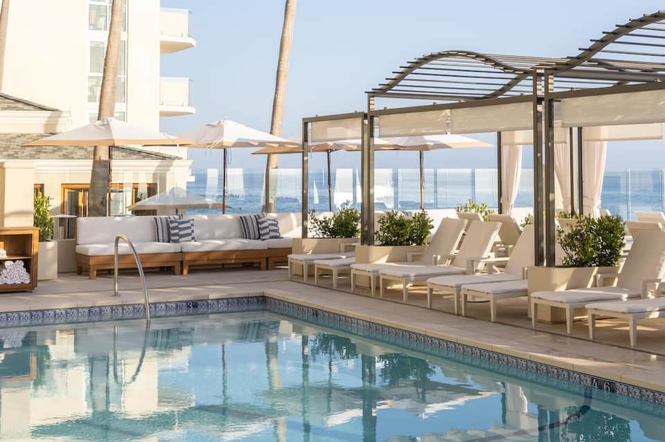 Rooftop pool terrace with ocean view, lounge seating, pergola shade, and white umbrellas