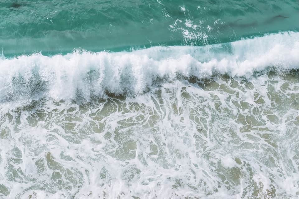 Aerial view of turquoise ocean waves with white foam breaking on sandy beach