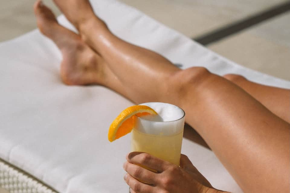 Close-up of hand holding cocktail with orange slice while relaxing on poolside lounge chair