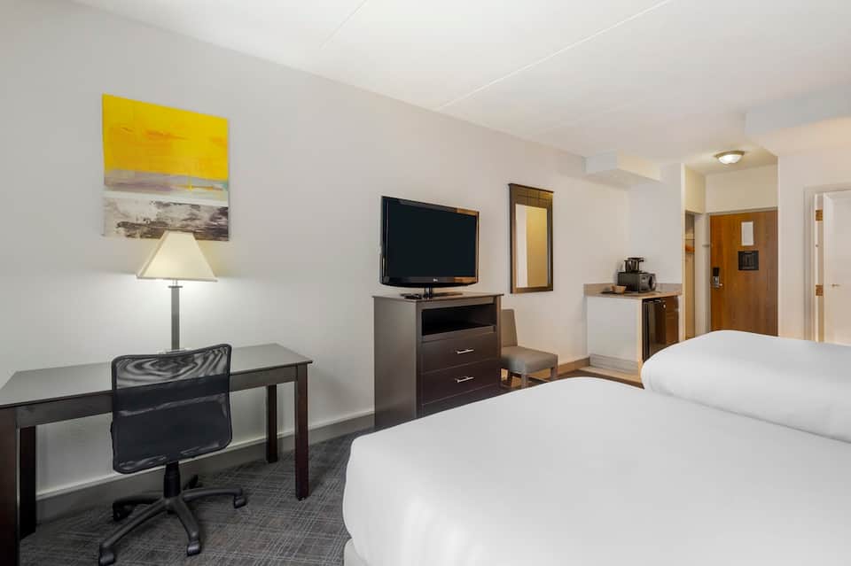 Hotel bedroom with two queen beds, desk, TV, lamp, and neutral color scheme with modern furnishings