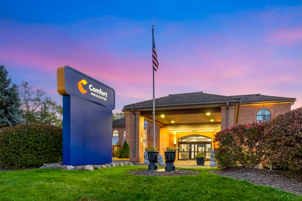 Comfort Inn hotel entrance at dusk with illuminated brick façade, flag, and manicured lawn