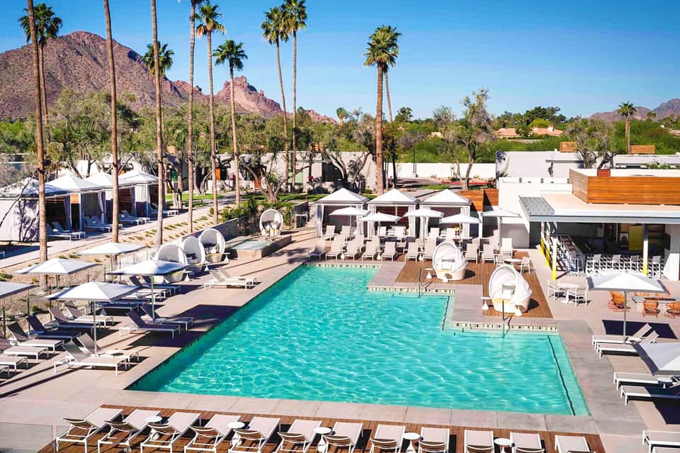 Modern resort pool with mountain views, loungers, umbrellas, and contemporary architecture