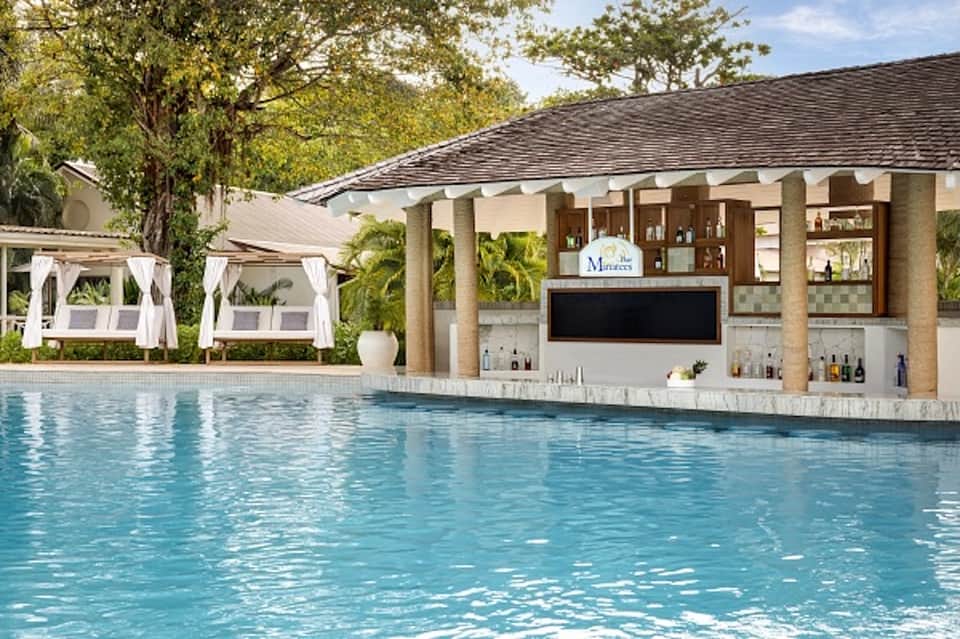 Resort pool bar with white cabanas, tropical landscaping, and covered pavilion