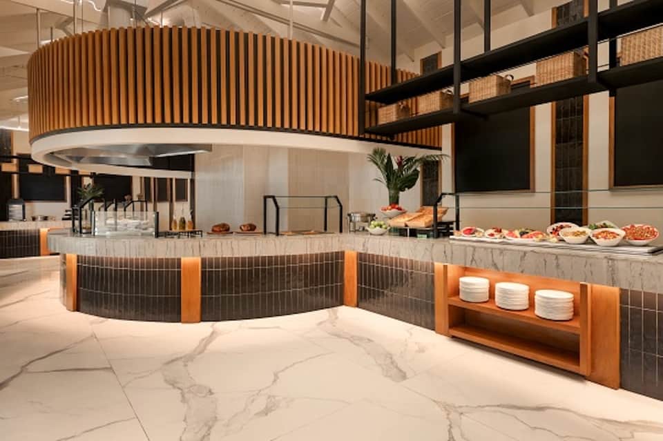Modern hotel restaurant with curved wooden ceiling, bar seating, and food display
