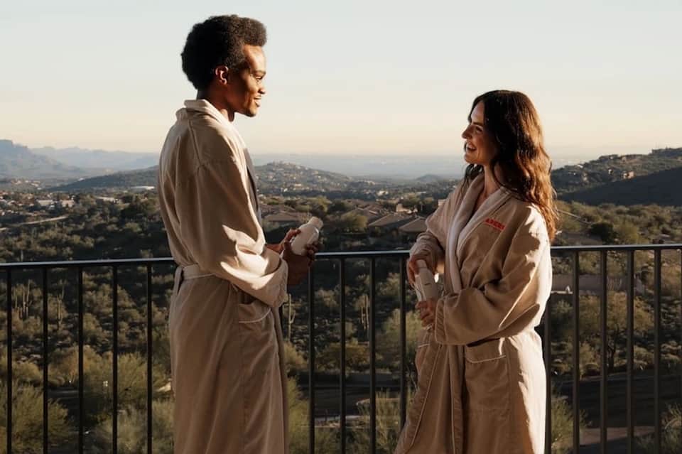 Two people in robes on a hillside terrace overlooking a scenic valley landscape