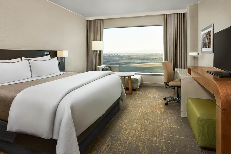Modern hotel room with city view, queen bed, work desk, and contemporary neutral décor