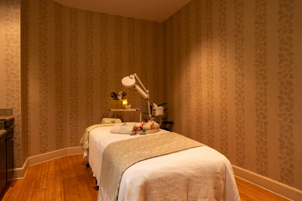 Spa treatment room with massage bed, gold-patterned wallpaper, and task lighting