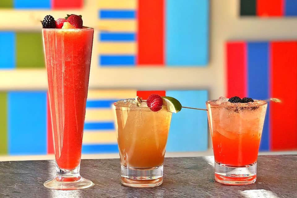 Three vibrant cocktails with fresh berries and citrus garnishes on colorful background