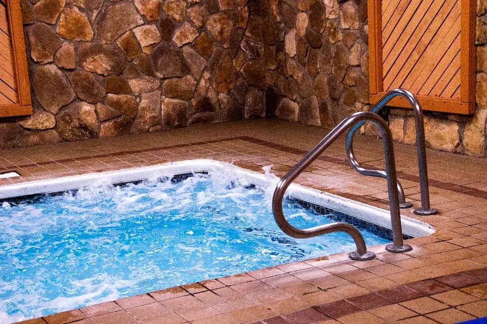 Indoor hot tub with metal handrails surrounded by stone walls and wooden doors