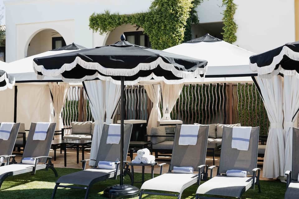 Elegant poolside cabanas with black and white umbrellas, curtains, and lawn seating area