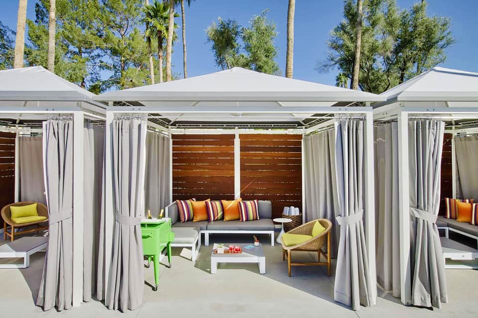 Luxury poolside cabanas with white canopies, curtains, cushioned seating, and palm trees