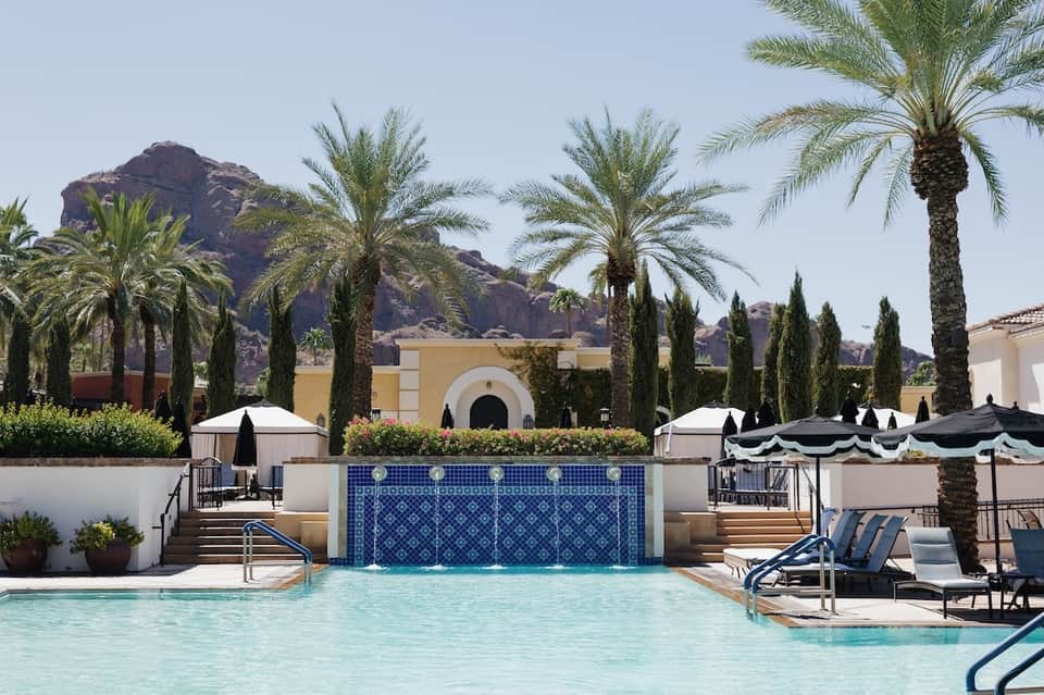 Resort pool with decorative blue tile waterfall, palm trees, and desert mountain backdrop