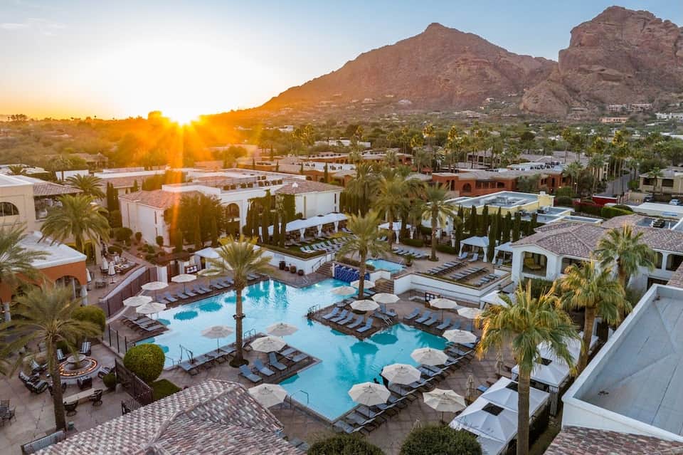 Resort pool complex at sunset with palm trees, lounge chairs, and mountain backdrop in desert