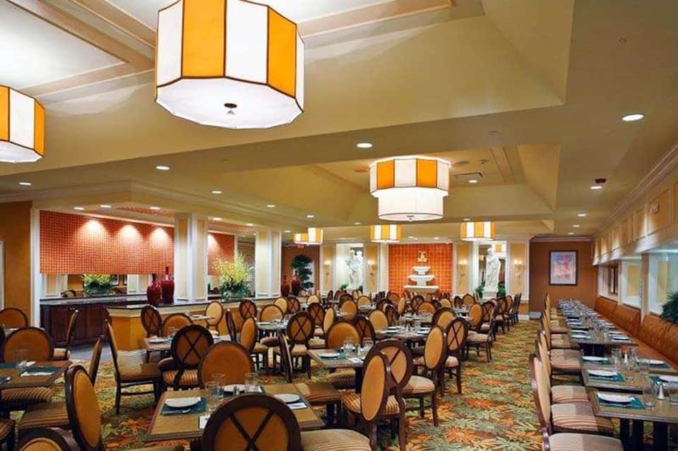 Elegant ballroom with round tables set for dining, orange striped lighting fixtures, and formal place settings
