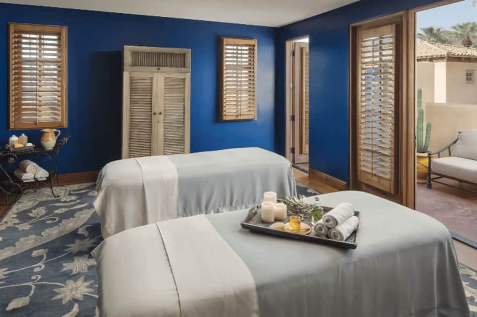 Spa massage room with blue walls, white massage tables, and relaxation amenities on tray