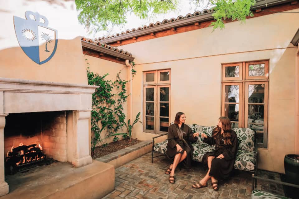 Two women sitting on patterned seating near outdoor fireplace in Mediterranean-style courtyard